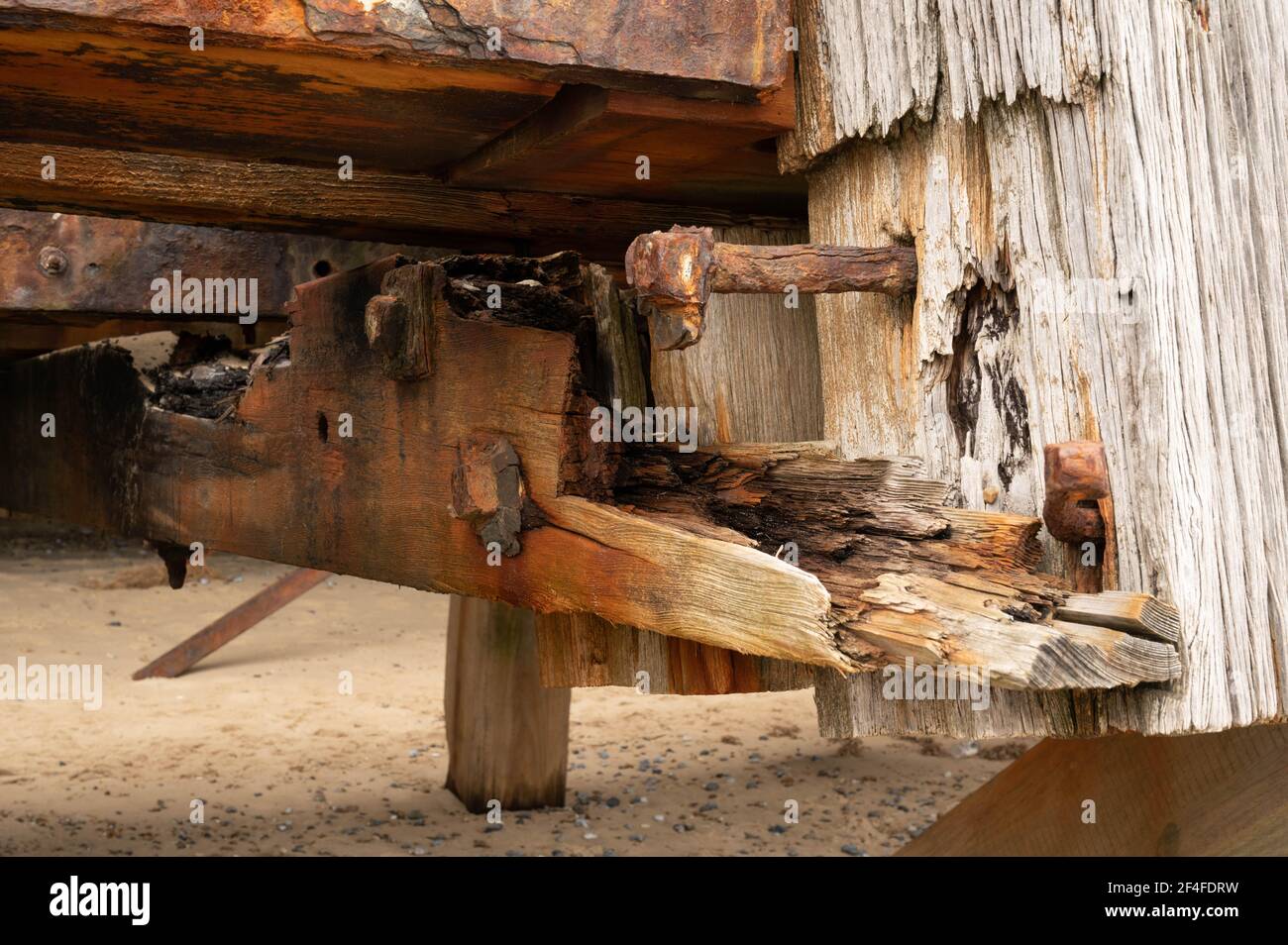 Travolgente travi di legno alla fine di un molo in inghilterra norfolk, dove l'aria e l'acqua di mare salato ha eroso e arrugginito tutti i dadi e bulloni grandi. Foto Stock