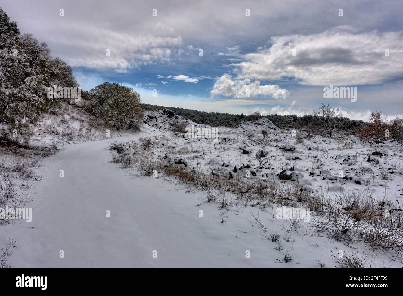 paesaggio invernale in sicilia con percorso innevato e antico pianura lavica contro il cielo drammatico Foto Stock