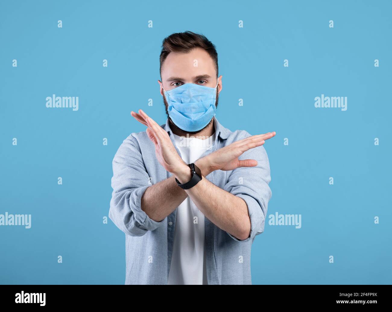 Lotta contro il coronavirus. Giovane uomo caucasico in maschera di faccia che gesturing STOP su sfondo blu studio Foto Stock