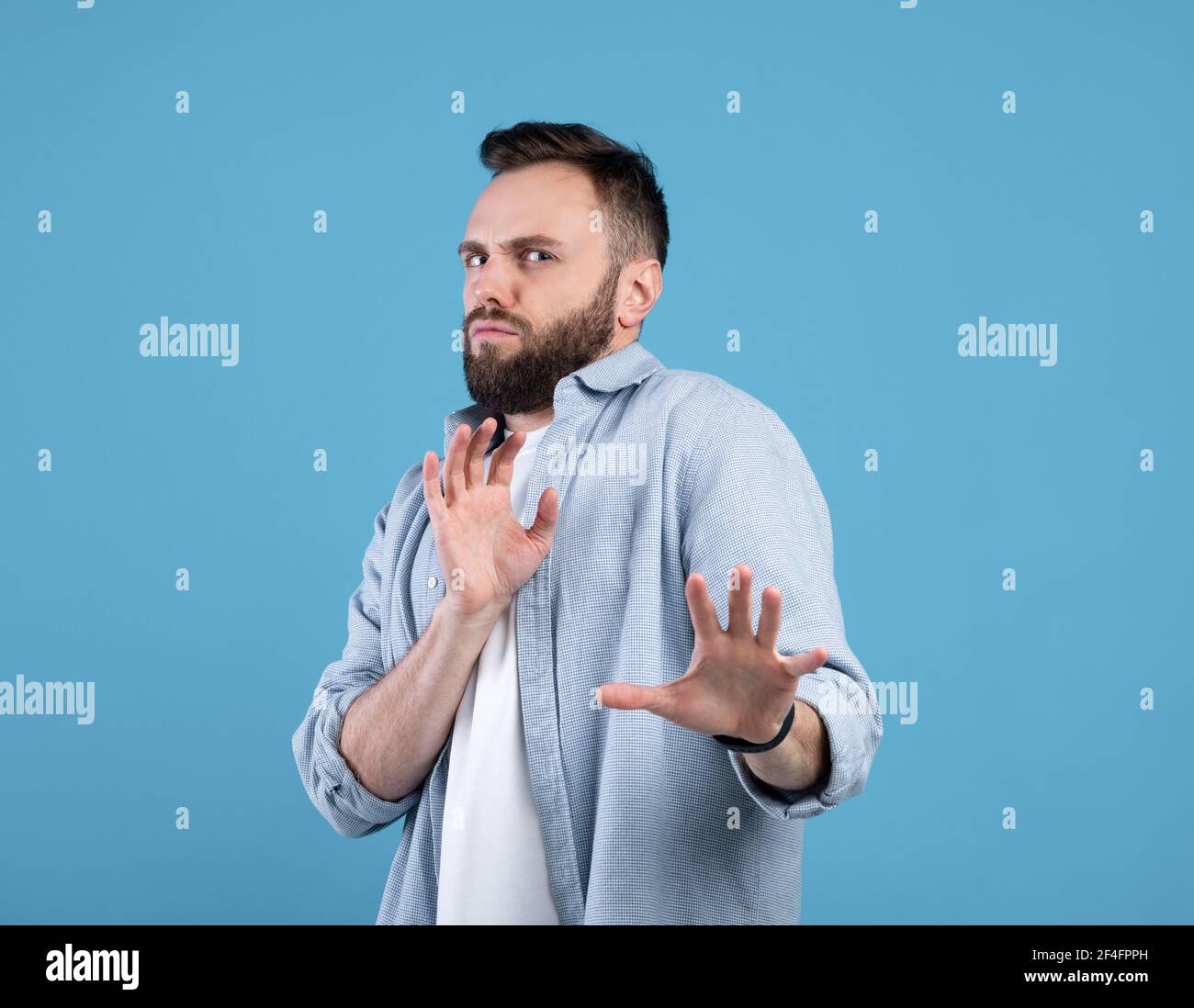 Un ragazzo millenario repulsato che rifiuta qualcosa, facendo UN gesto DI STOP sullo sfondo blu dello studio Foto Stock