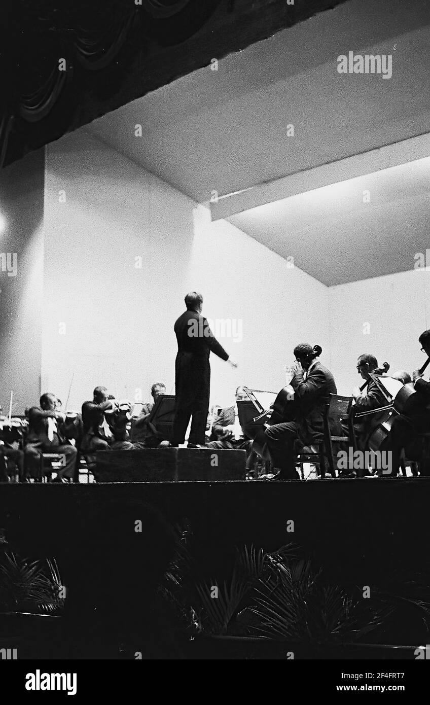 Vista ad angolo basso di un direttore, dal retro, che guida una grande orchestra su un palco, l'Avana, Cuba, 1964. () Foto Stock