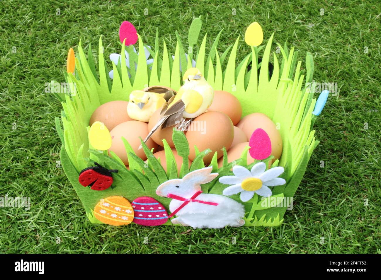 Sfondo decorativo di Pasqua. Cestino pasquale in feltro pieno di uova di pollo isolato su sfondo erba Foto Stock