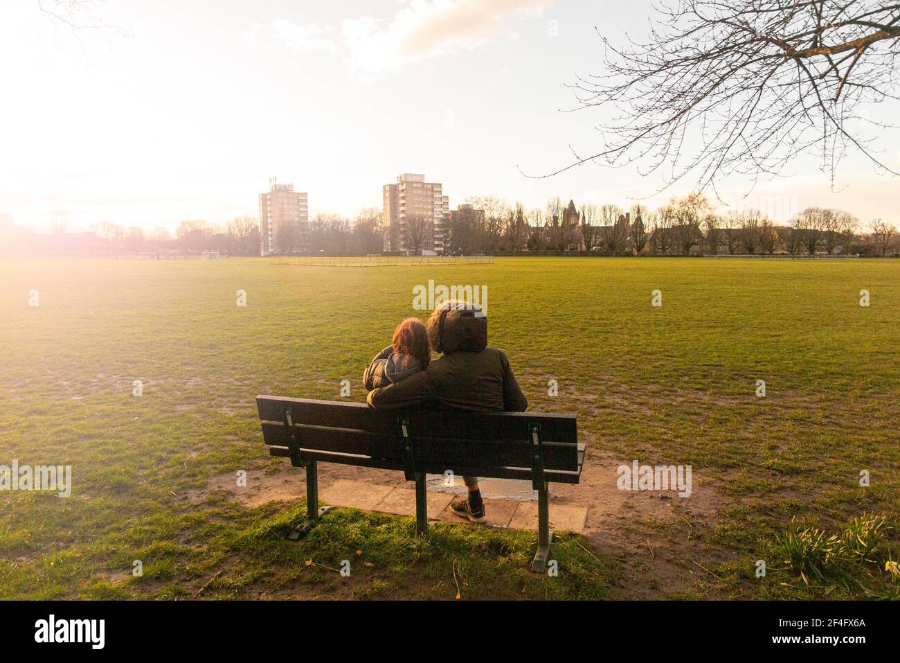 Una coppia seduta su una panchina in un parco urbano A Londra al sole del pomeriggio Foto Stock