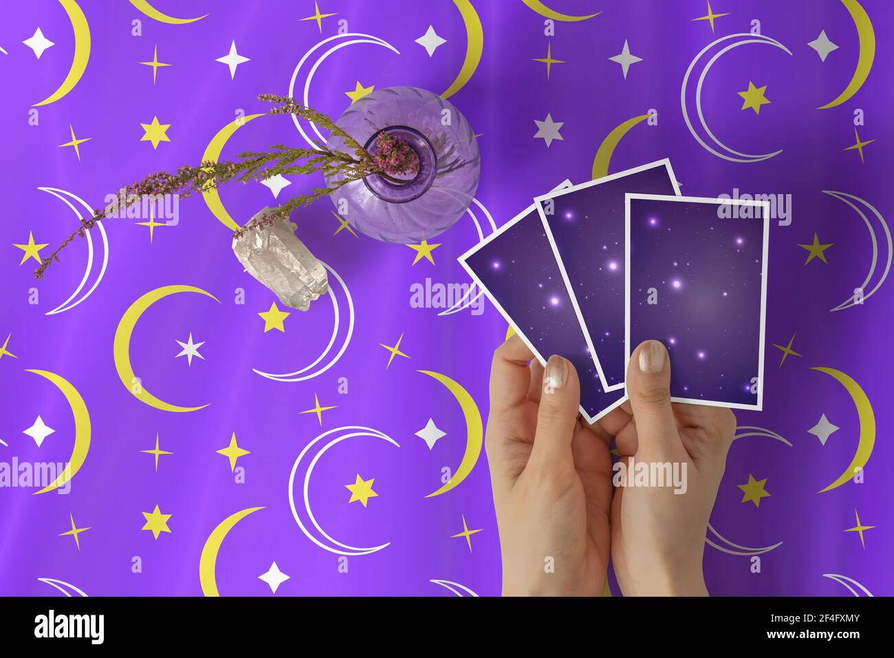 Mani di giovane donna con smalto dorato del chiodo che tiene tre carte del tarocco o dell'oracolo, su una tela di tabella delle stelle viola e del modello di mezzaluna Foto Stock