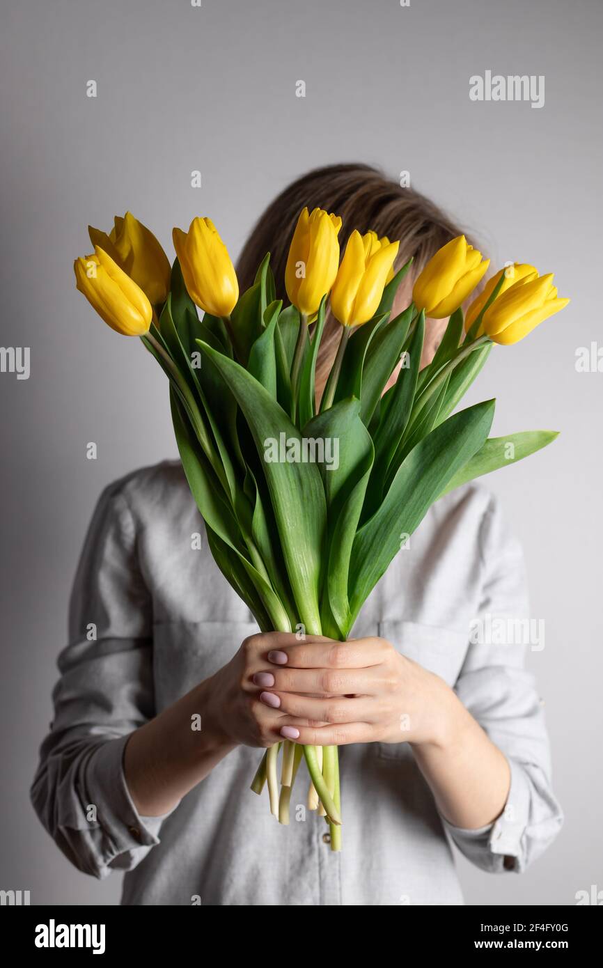 Donna che tiene bouquet di tulipani gialli e si nasconde dietro di esso Foto Stock