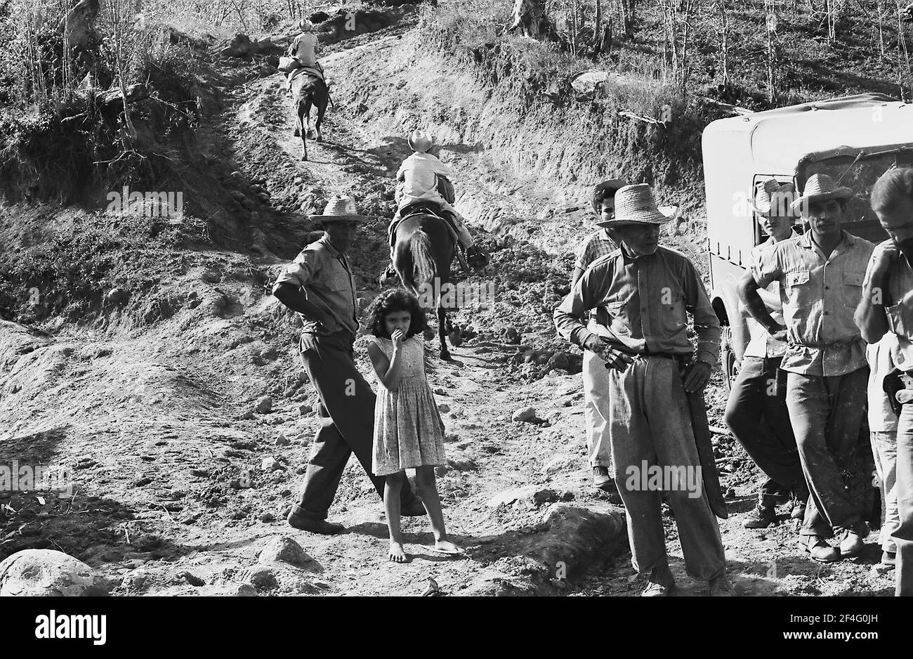 La gente è visibile in una strada sterrata con un veicolo in stile jeep mentre scende dalle montagne della Sierra Maestra, Cuba, 1963. Dalla collezione di fotografie Deena Stryker. () Foto Stock
