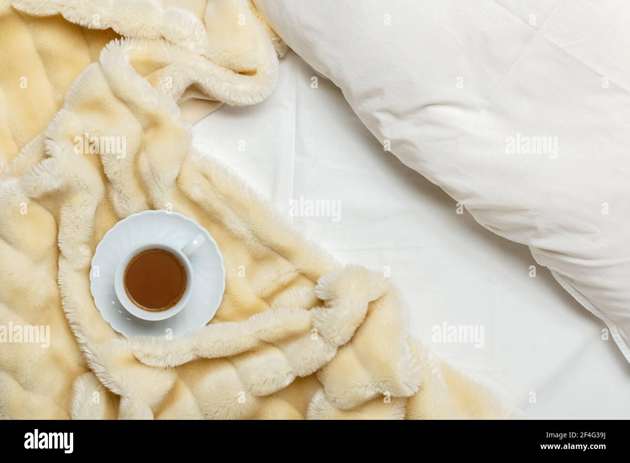 Vista dall'alto della colazione in camera. Mattina accogliente. Lenzuola bianche, una soffice coperta beige e una tazza di caffè. Foto Stock