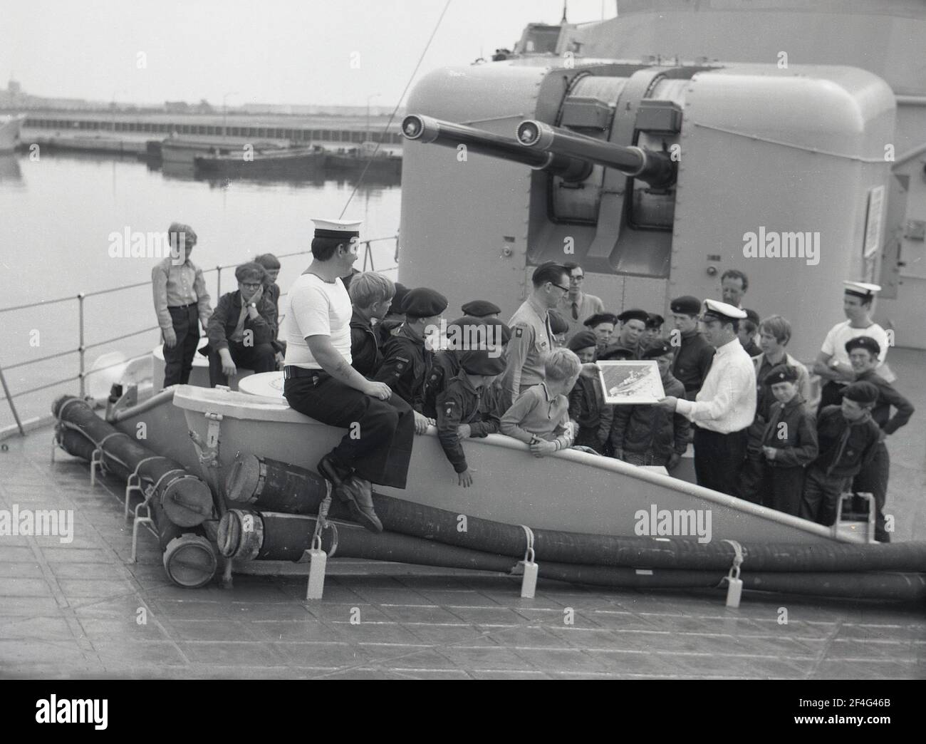 1970, a bordo della HMS Ajax, il capitano della nave che mostra una foto ai cucciolo scout visitando la nave da guerra Royal Naval ormeggiata nel molo di Devonport, Plymouth, Inghilterra, Regno Unito. Foto Stock