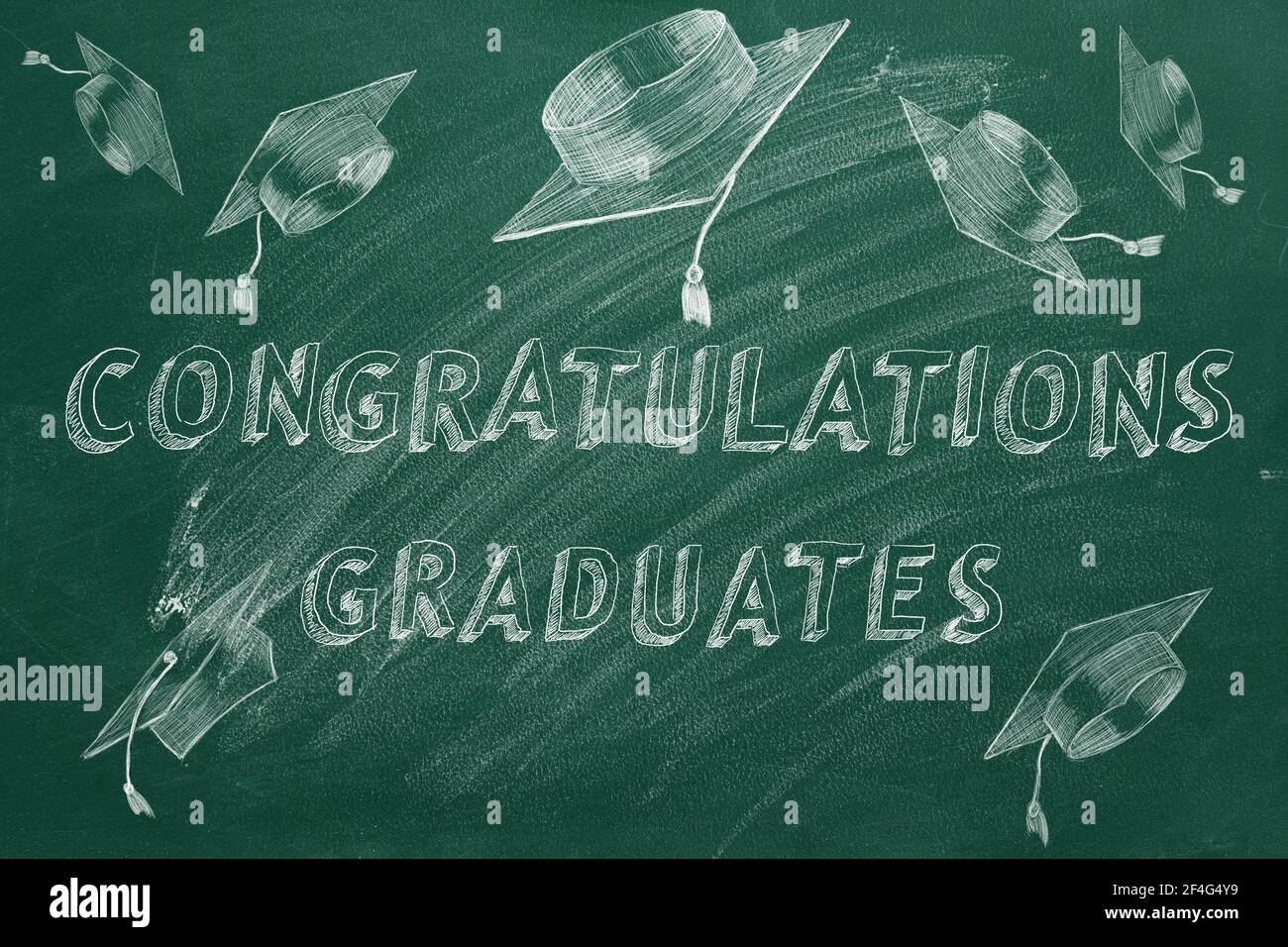 Testo di disegno a mano 'congratulazioni laureati' e tappi di laurea su lavagna verde. Foto Stock