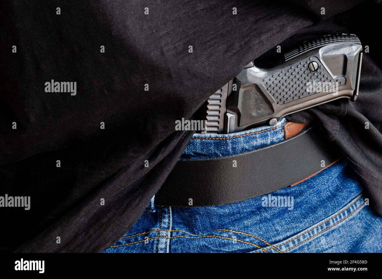 Una persona sta nascondendo una pistola sotto la cintura di denim. Pistola  con diramatore sotto la cintura in denim Foto stock - Alamy