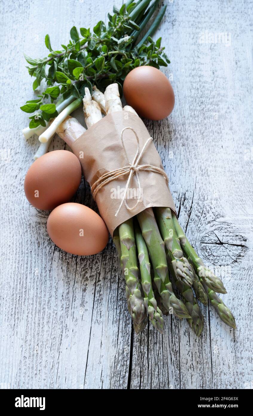 Gruppo di asparagi crudi con uova, cipolle ed erbe su sfondo ligneo. Direttamente sopra. Foto Stock