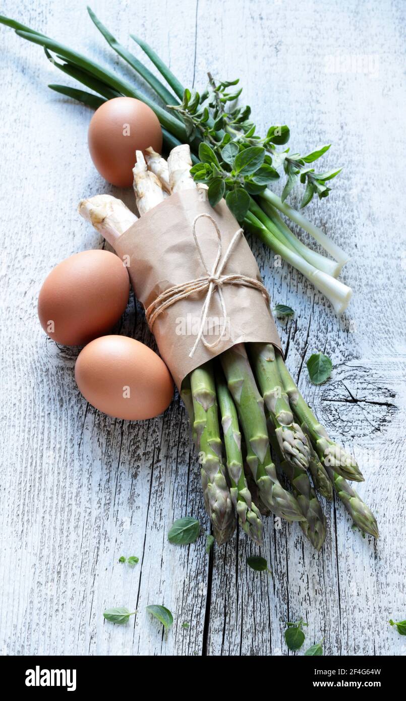 Gruppo di asparagi crudi con uova, cipolle ed erbe su sfondo ligneo. Direttamente sopra. Foto Stock