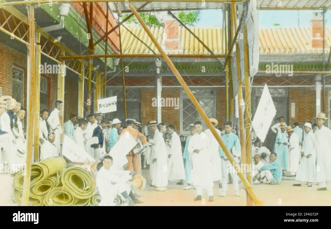 Un gruppo di manifestanti studenteschi, associati al movimento del quarto maggio, si laminarono intorno ad un cortile aperto in una giornata di sole, con rotoli di stuoia tessuta in primo piano, Pechino, Cina, 1919. Dalla collezione di fotografie di Sidney D. Gamble. () Foto Stock