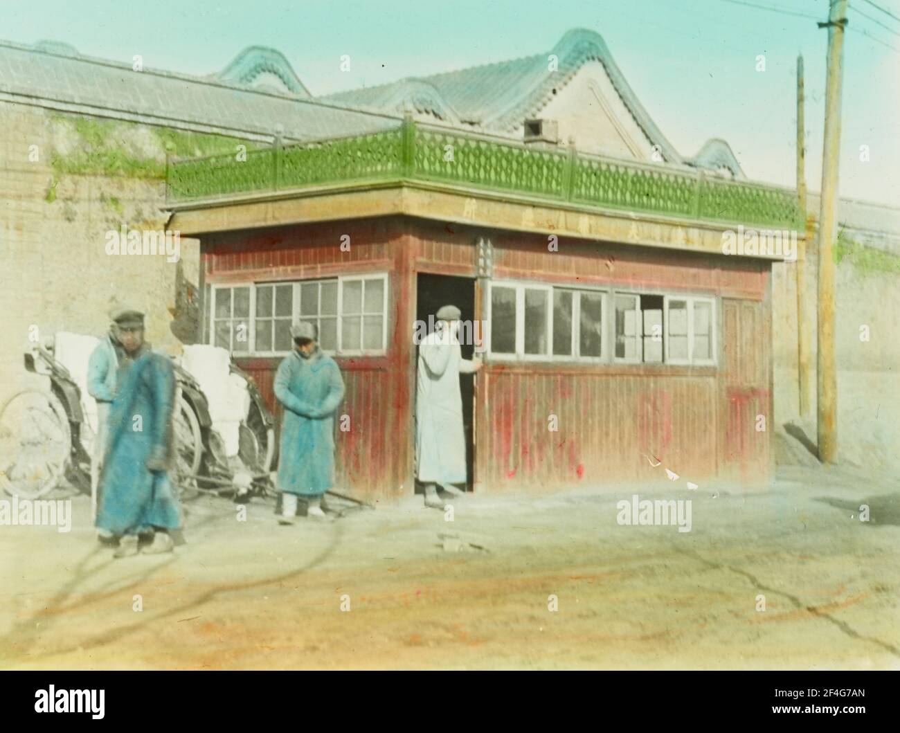 Molti uomini che indossano cappotti lunghi, in una giornata di sole, si trovano su una strada sterrata vicino a un rickshaw conducente 'rifugio, Pechino, Cina, 1918. Dalla collezione di fotografie di Sidney D. Gamble. () Foto Stock