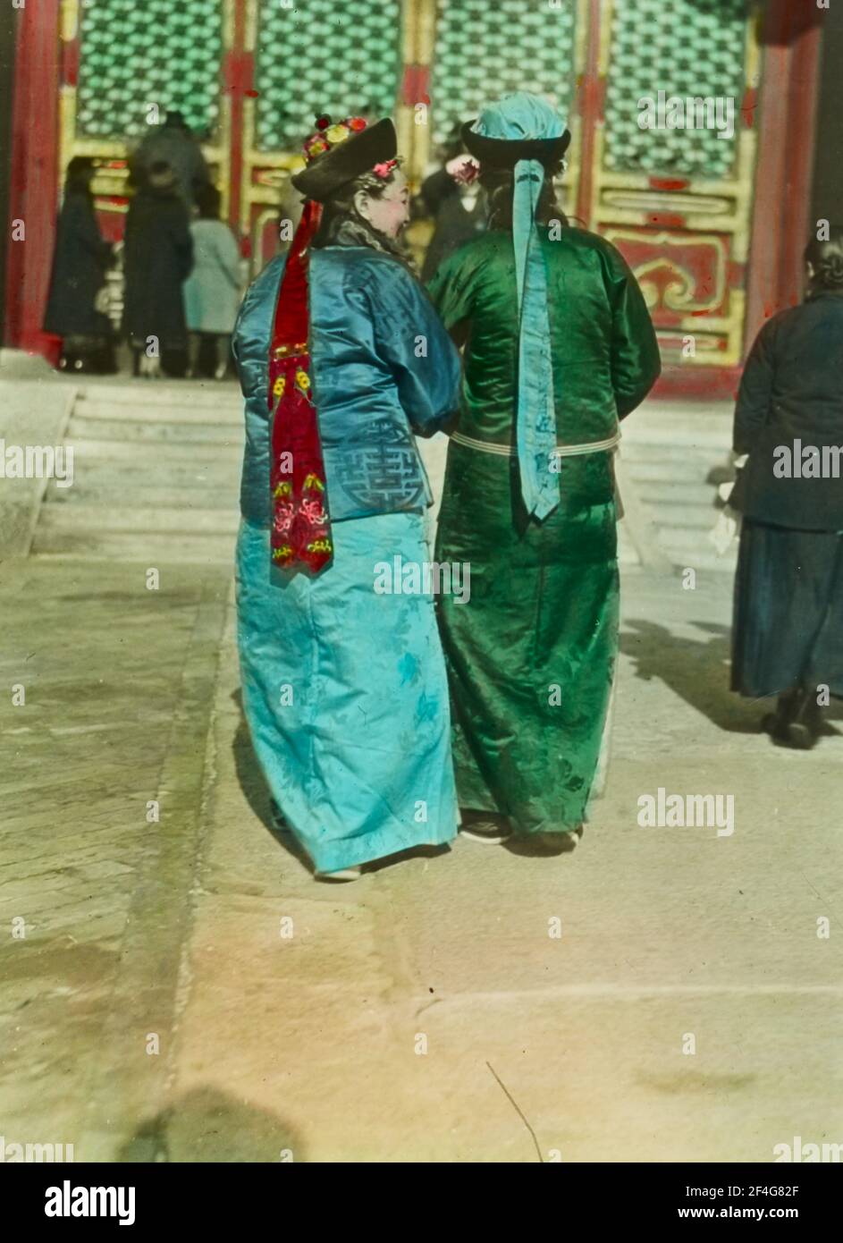 Foto a tutta lunghezza di due donne manchu della dinastia Qing, dalla parte posteriore, con acconciature liangbatou moderate mentre attraversi un cortile soleggiato nella Città Proibita, Pechino, Cina, 1918. Dalla collezione di fotografie di Sidney D. Gamble. () Foto Stock