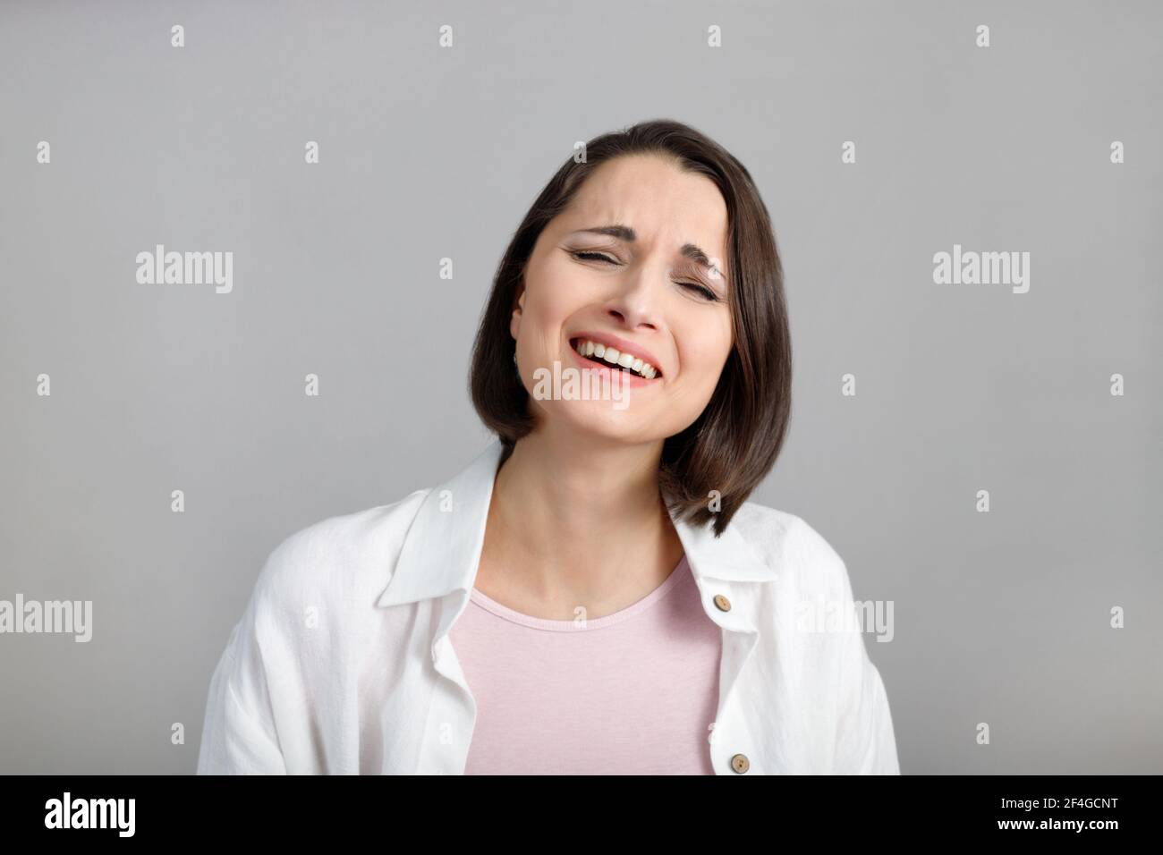 Espressioni ed emozioni del volto umano. Ritratto di giovane donna multietnica di bruna ridente in canotta rosa e camicia bianca. Foto Stock