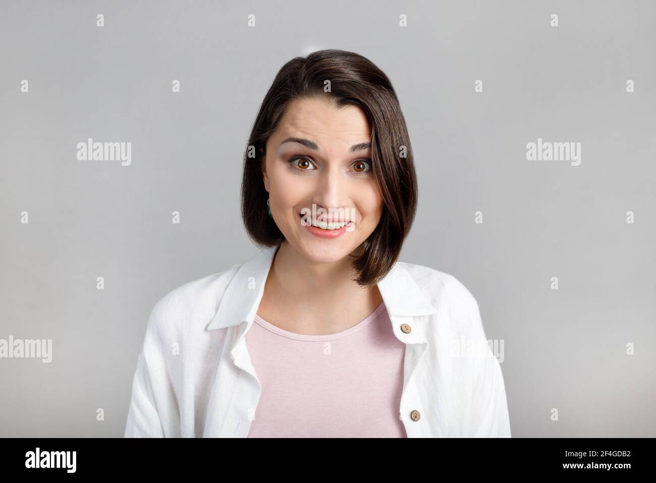 Espressioni ed emozioni del volto umano. Ritratto di giovane donna di brunetta in tanica rosa e camicia bianca guardando la macchina fotografica. Foto Stock