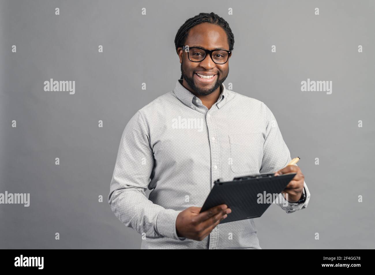 Afroamericano ora dipendente in una camicia formale con occhiali in piedi con appunti neri, positività - l'arma segreta per aumentare la produzione, controlla l'elenco dei compiti, interviste per il lavoro Foto Stock