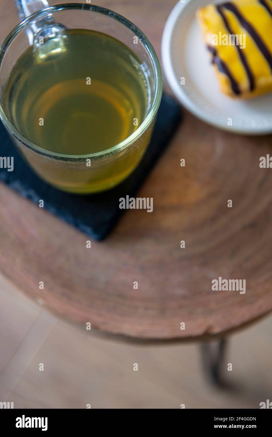 Un bicchiere di tè verde e una torta gialla su un piccolo tavolo di legno Foto Stock