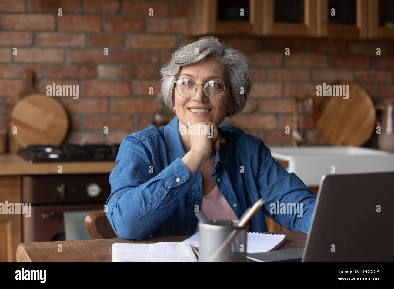 Sognante anziano studio donna da casa uso notebook sorriso immaginare Foto Stock