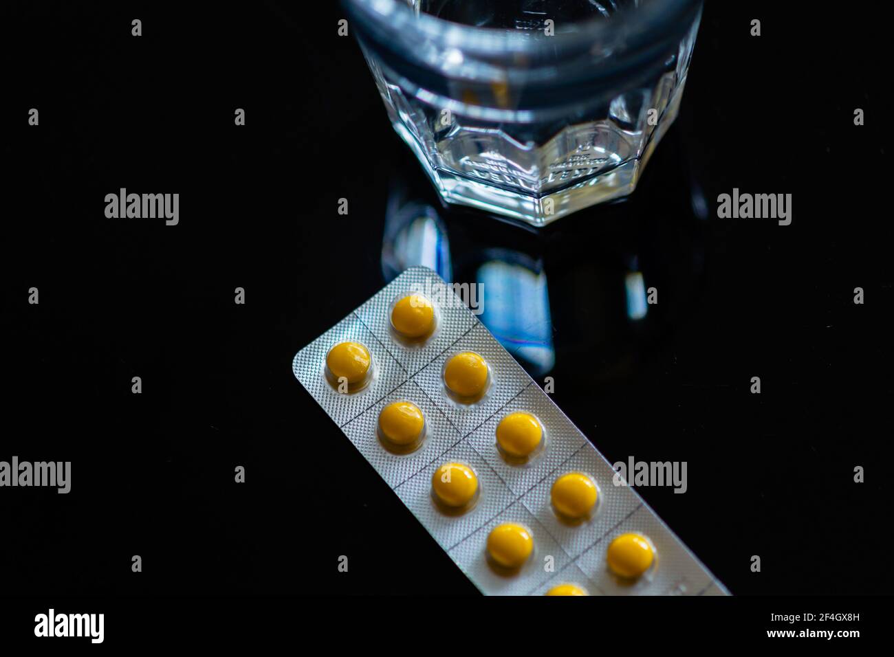 Compresse gialle in blister vicino al bicchiere d'acqua su sfondo nero Foto Stock
