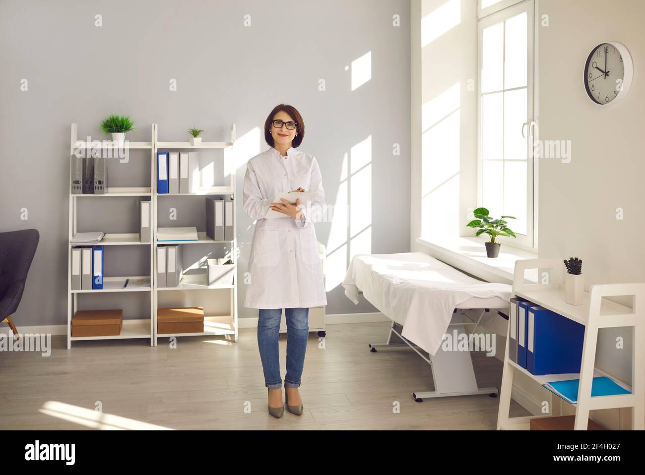 Donna amichevole che lavora come medico si trova in ufficio e guarda la fotocamera sorridente. Foto Stock