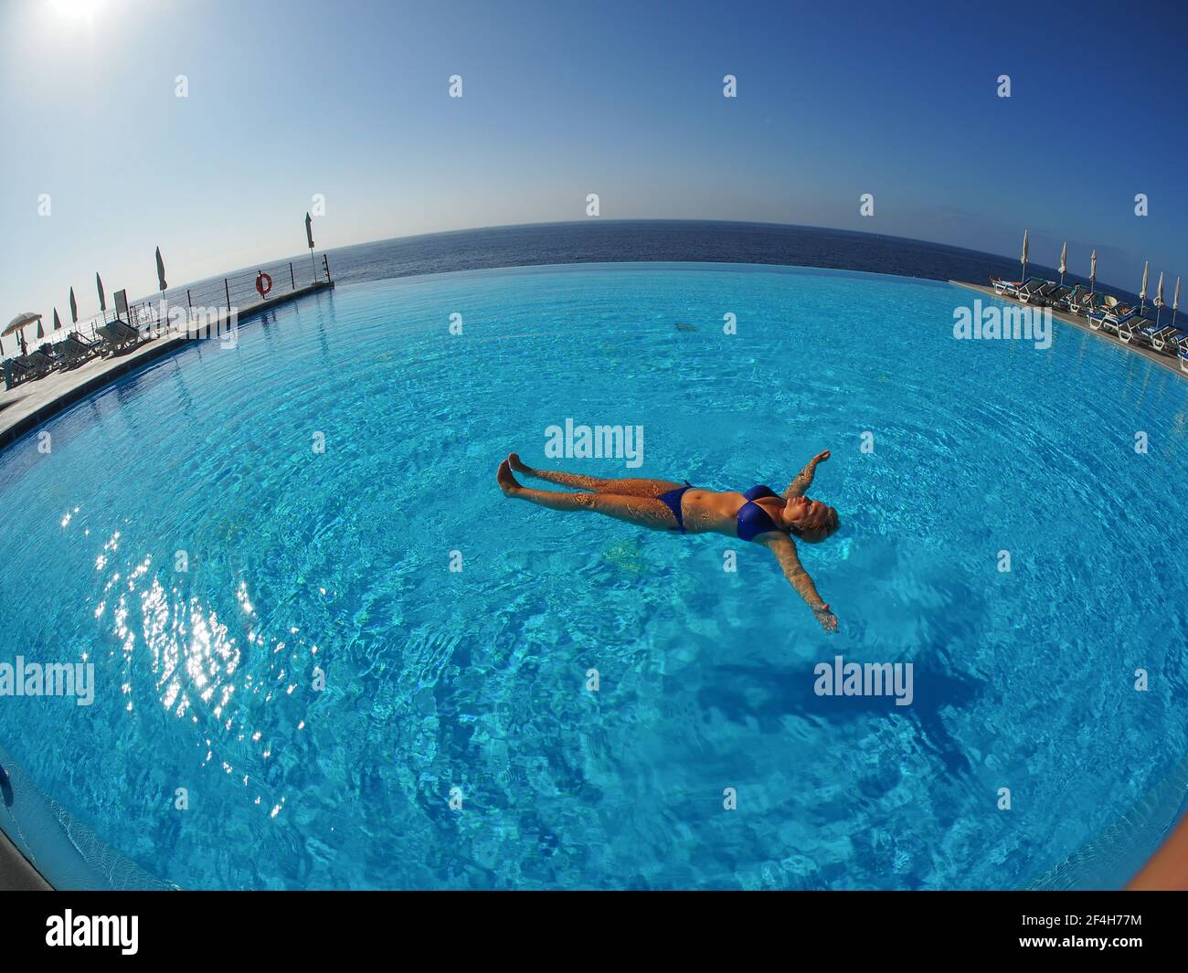 Madera, Portogallo. 09,05,2017 Donna in bikini blu che galleggia da sola in una piscina al sole, di fronte al mare sull'isola di Madeira. Foto Stock