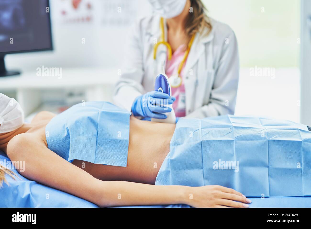 Medico in maschera che fa test ecografico dell'addome alla paziente femminile Foto Stock