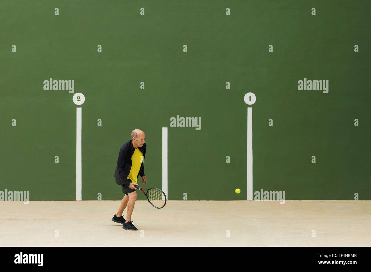 Atleta maschile anziano che colpisce palla con racchetta mentre si gioca a  tennis contro parete verde in palestra Foto stock - Alamy