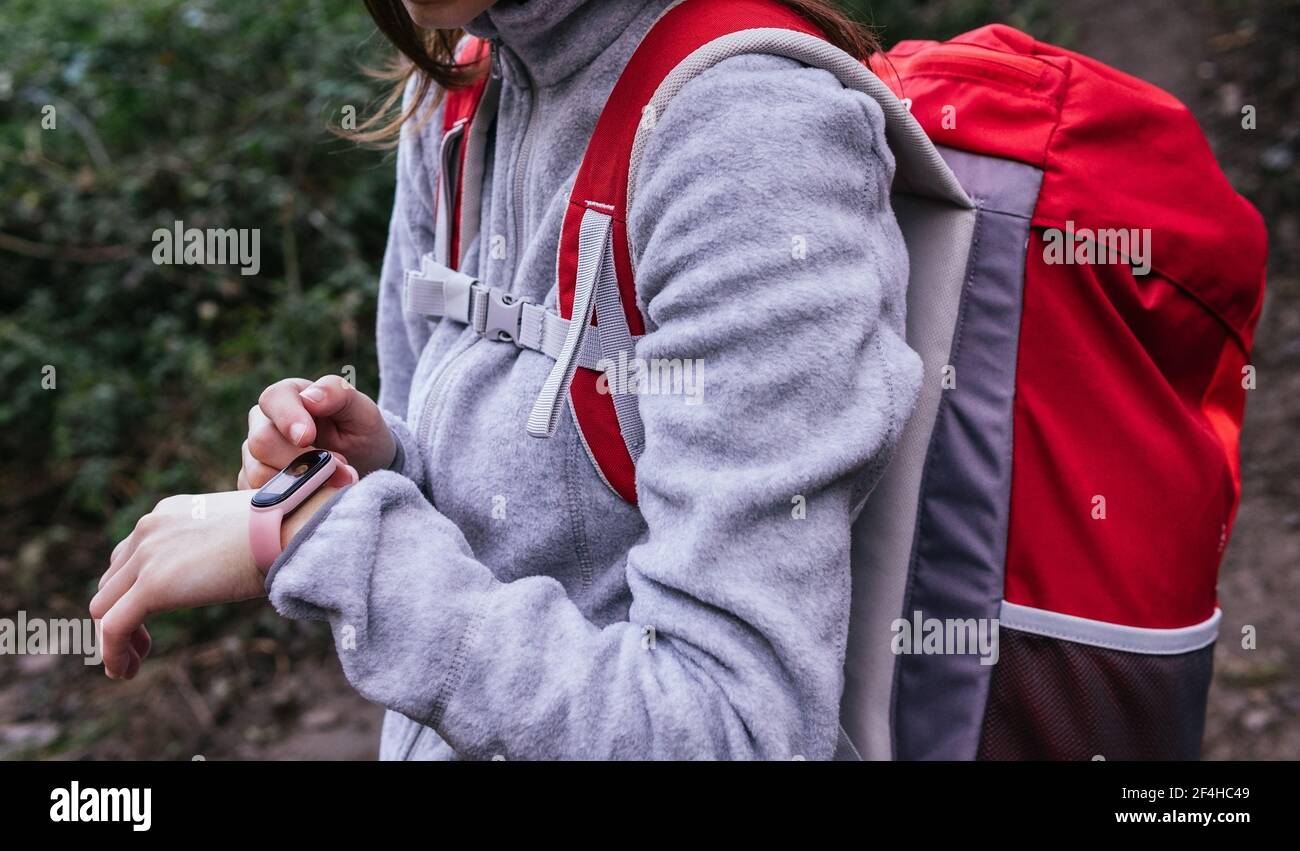 Vista laterale del prodotto femmina in activewear con zaino usando GPS su fitness tracker per la navigazione durante le escursioni nella foresta Foto Stock