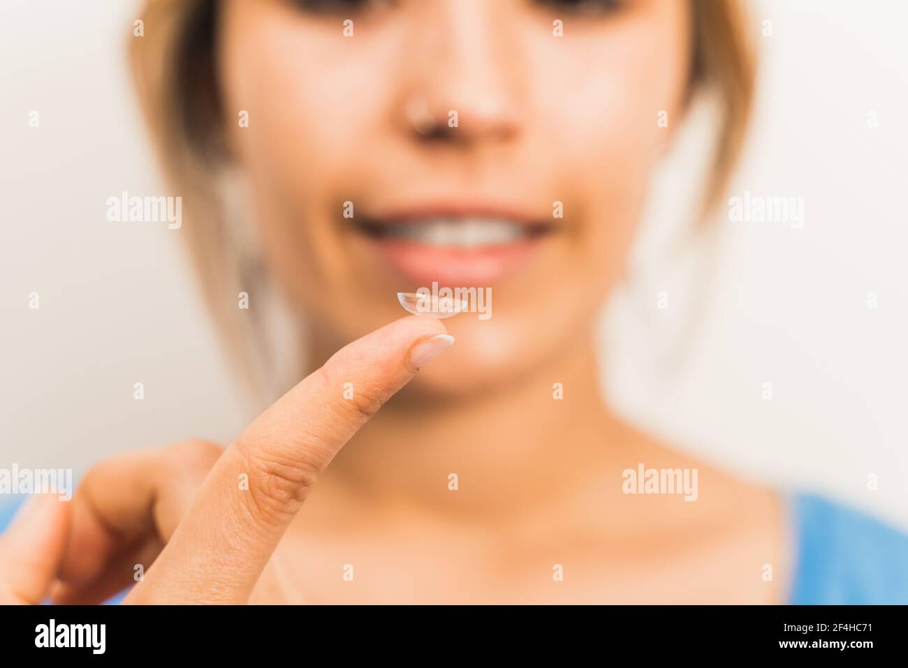 Crop blurred sorridente femmina preparandosi a mettere in contatto lente sulla punta delle dita in un ambiente luminoso Foto Stock