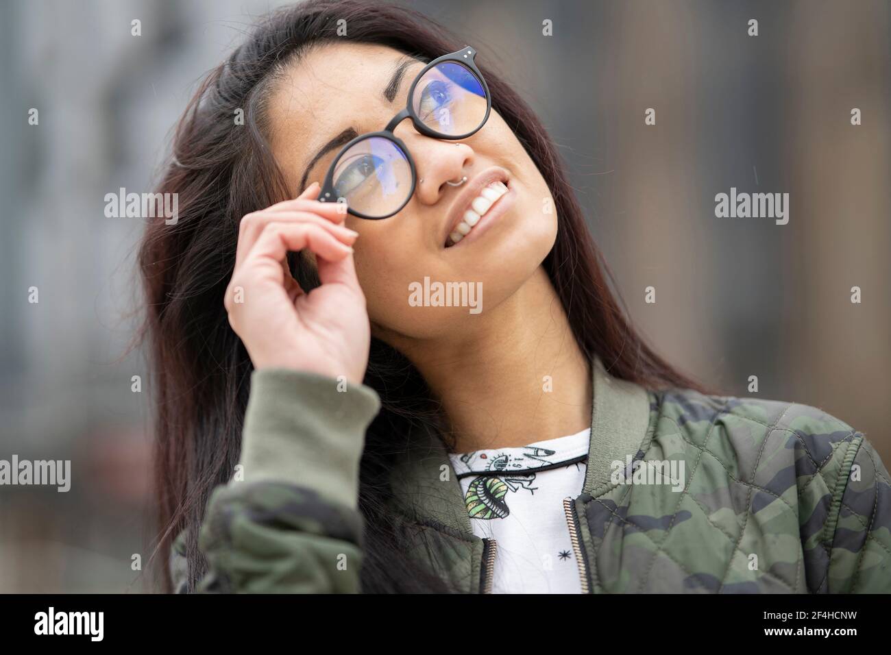 Affascinante donna asiatica concentrata utilizzando arricciacapelli sulle ciglia mentre si fa il trucco di fronte allo specchio a casa Foto Stock