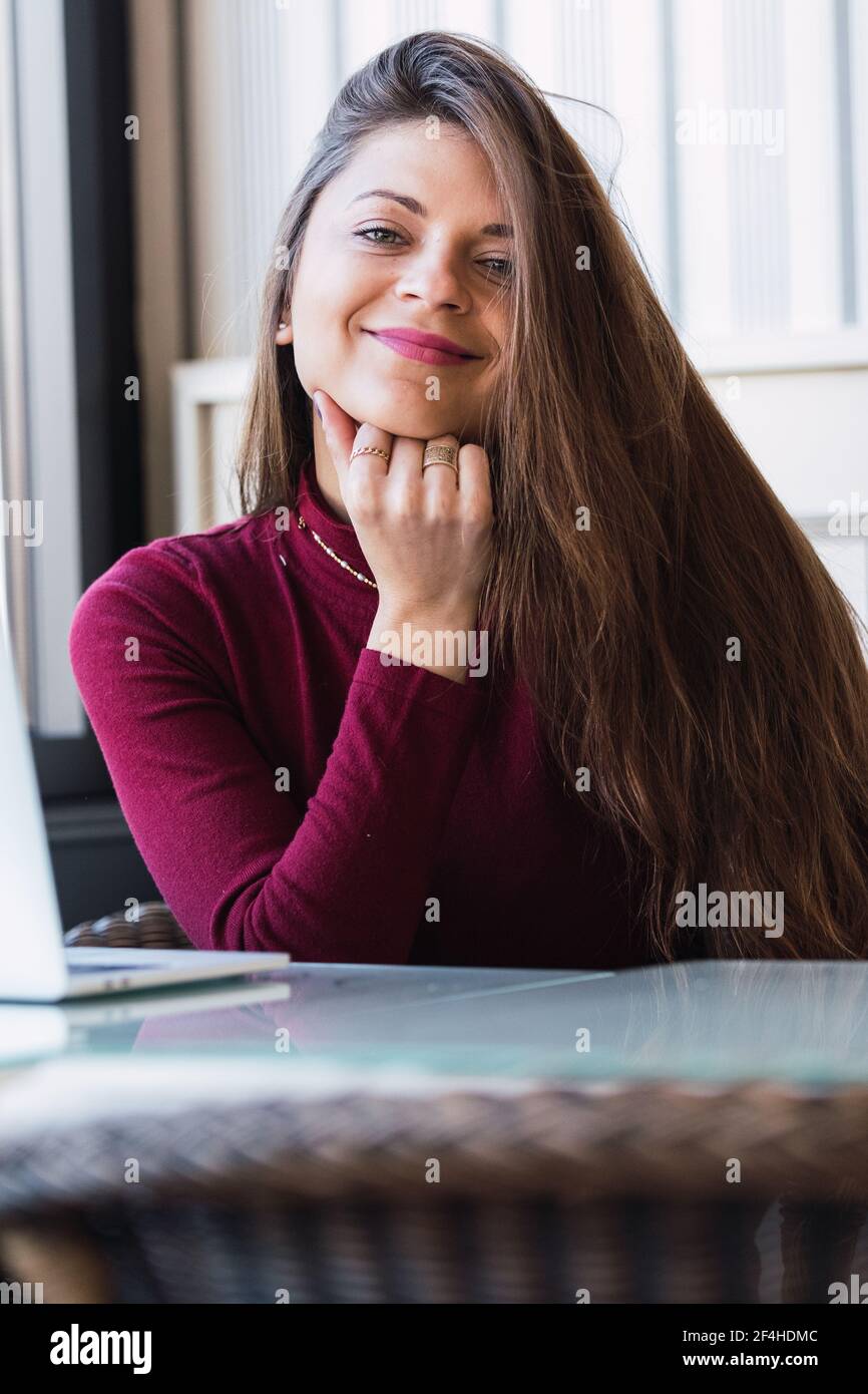 Felice elegante donna dai capelli lunghi sorridente e guardando la macchina fotografica mentre si riposa in un caffè Foto Stock