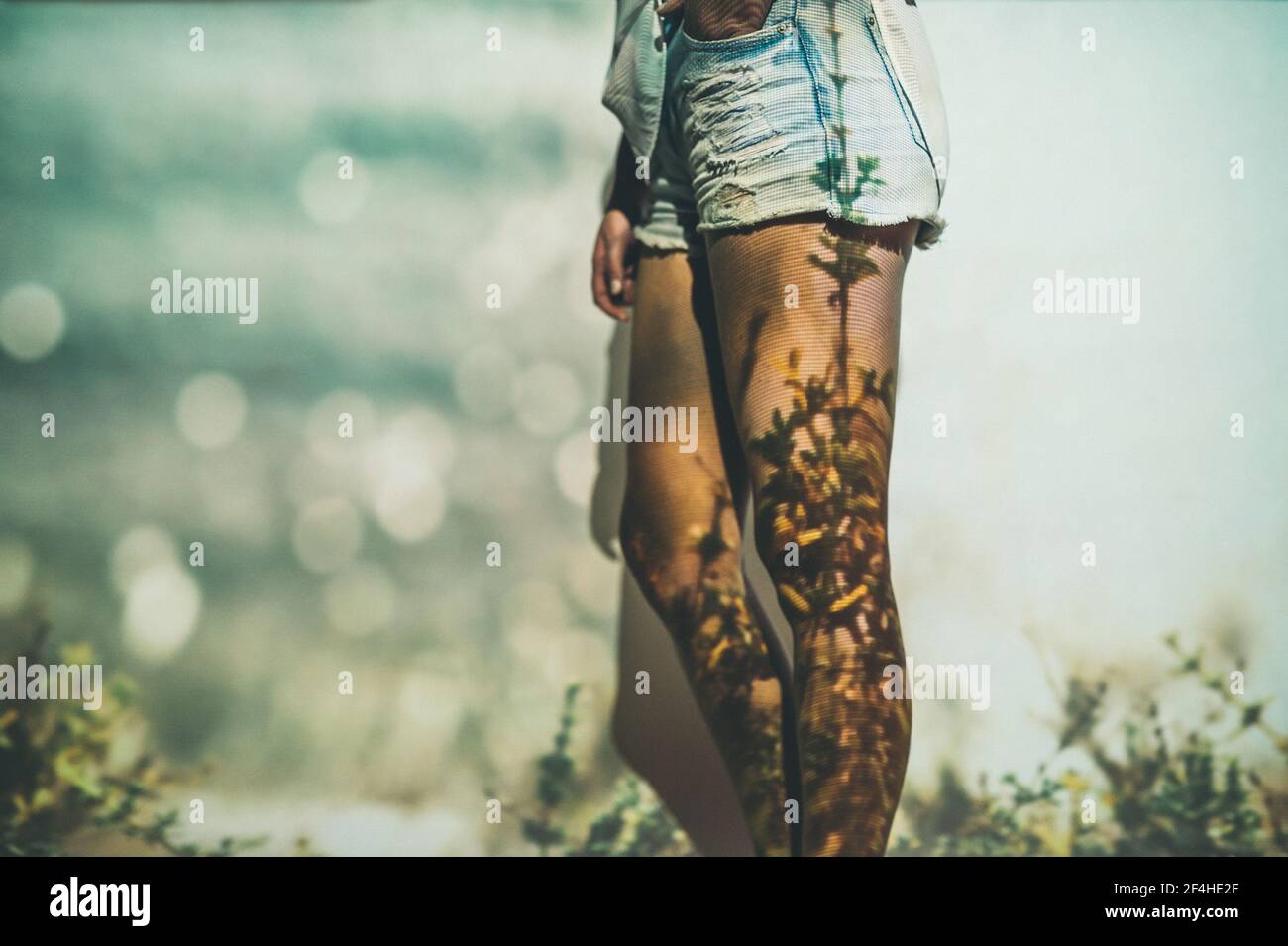 Donna irriconoscibile in eleganti shorts in piedi vicino alla parete con proiezione di erba in estate Foto Stock