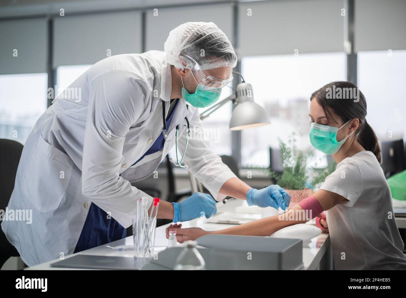 Una giovane donna è venuta in laboratorio per donare sangue da una vena, una giovane assistente di laboratorio prende il sangue Foto Stock