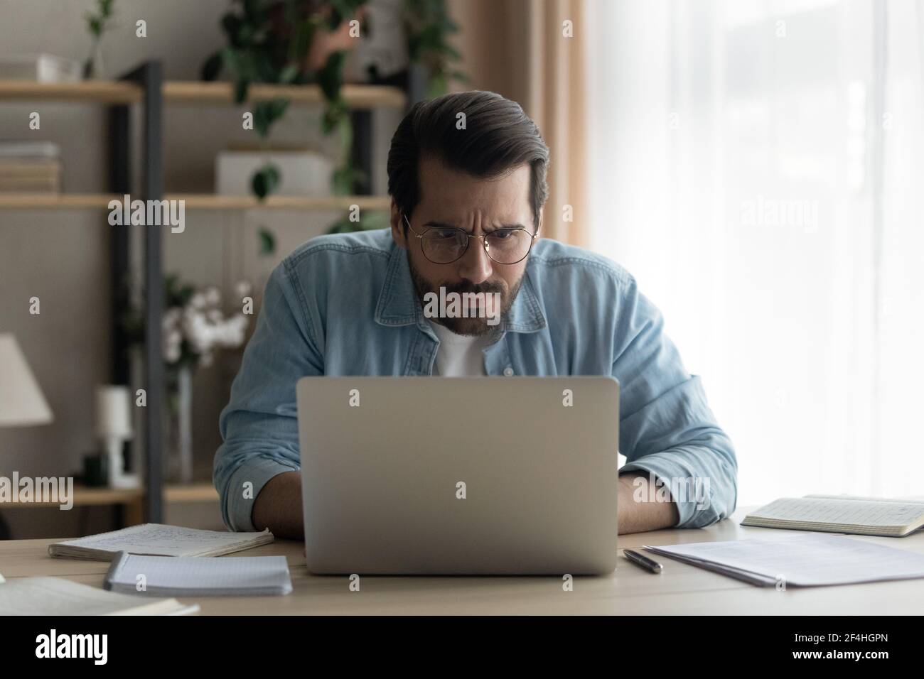 Primo piano uomo d'affari perplesso che indossa occhiali guardando lo schermo del notebook Foto Stock