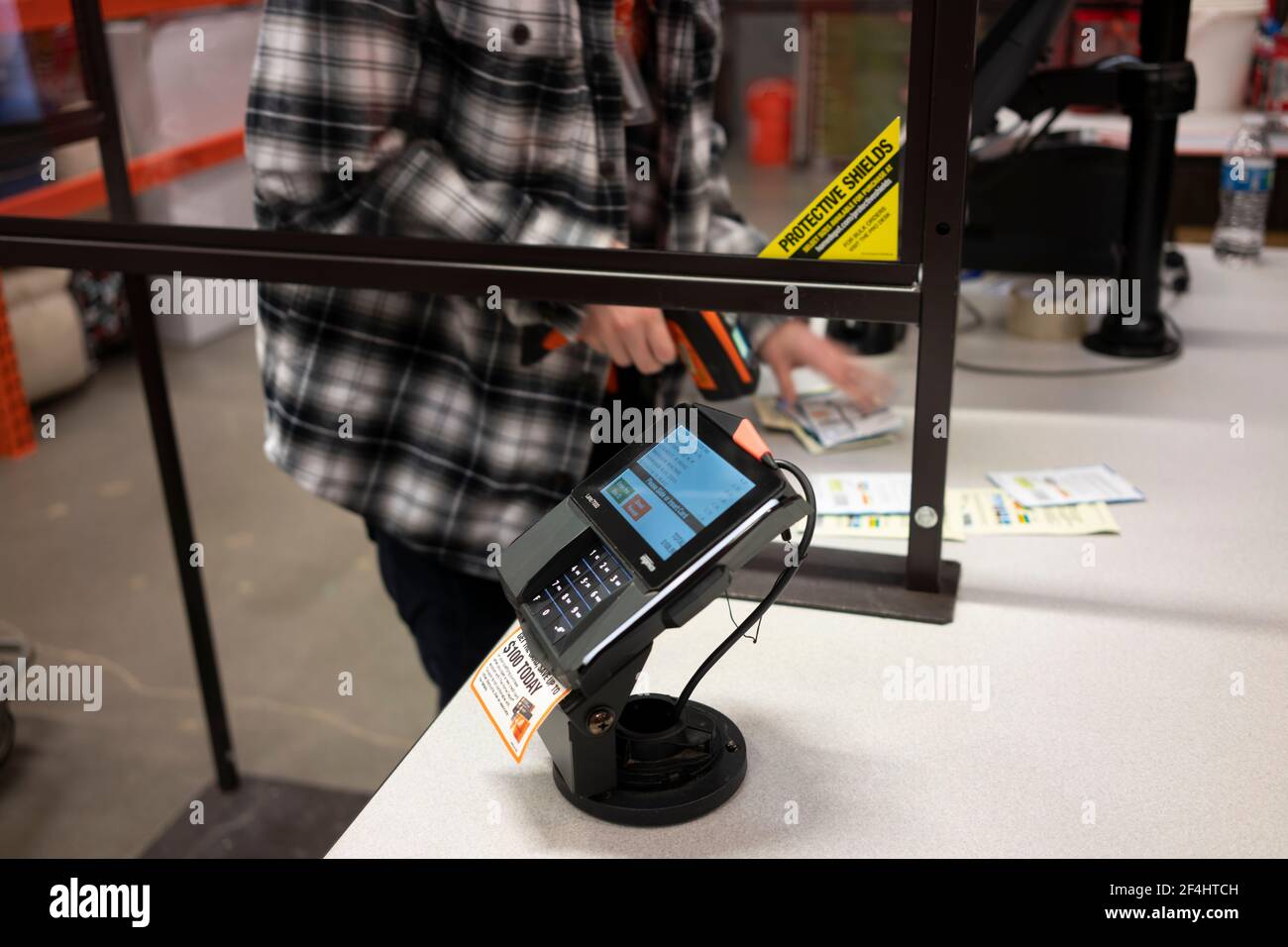 Closeup del tastierino PIN Ingenico Lane 7000 nella corsia di cassa con un cassiere in background utilizzando un lettore di codici a barre dietro lo schermo in casa... Foto Stock