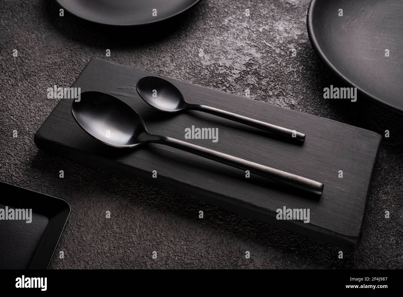 cucchiai neri opachi e circondati da piatti e utensili su cemento scuro.  concetto per un ristorante o un caffè, una caffetteria Foto stock - Alamy