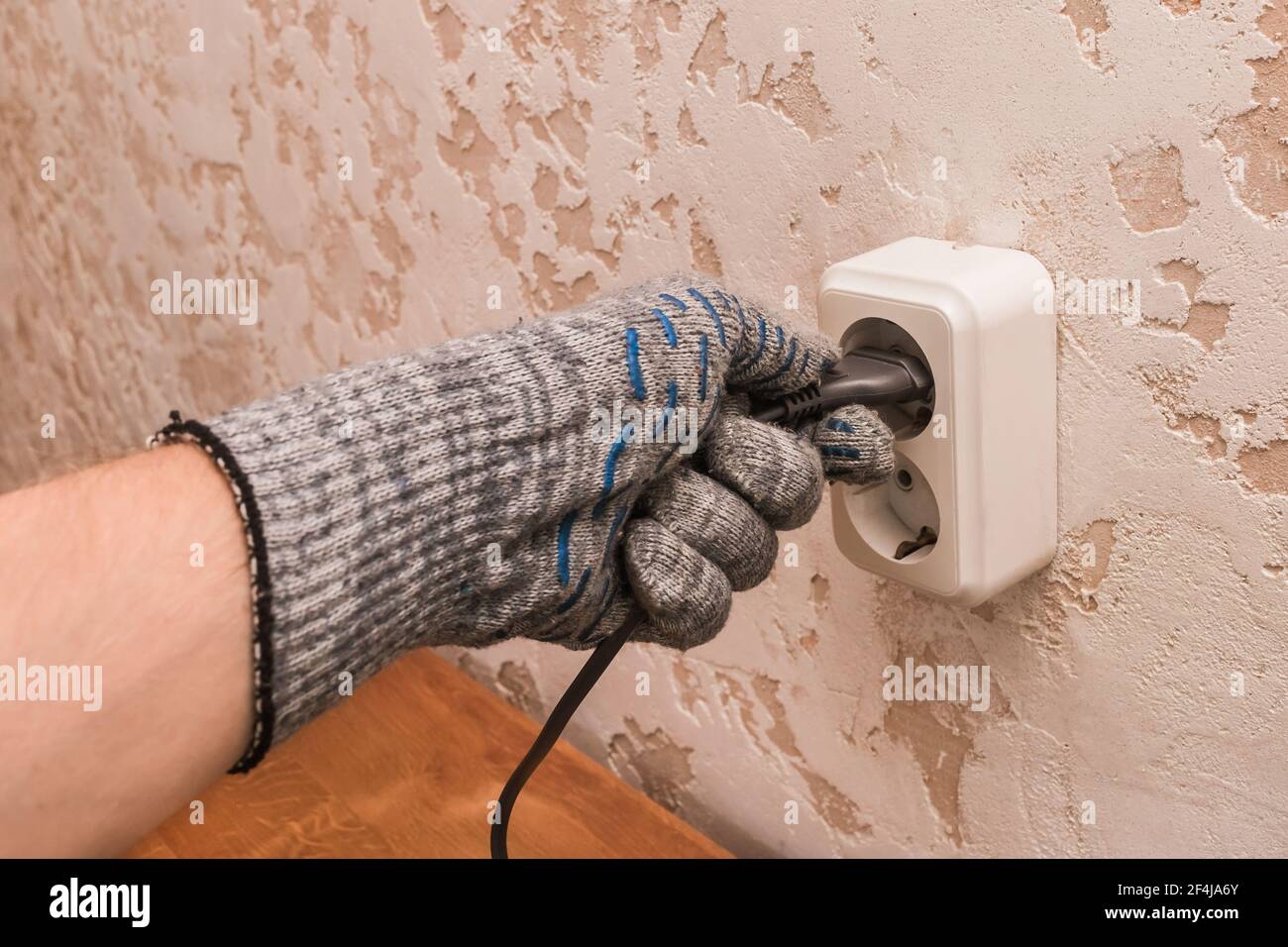 La mano di un addetto alla costruzione in guanti protettivi collega una spina a una presa doppia sullo sfondo di un ambiente interno moderno. Foto Stock