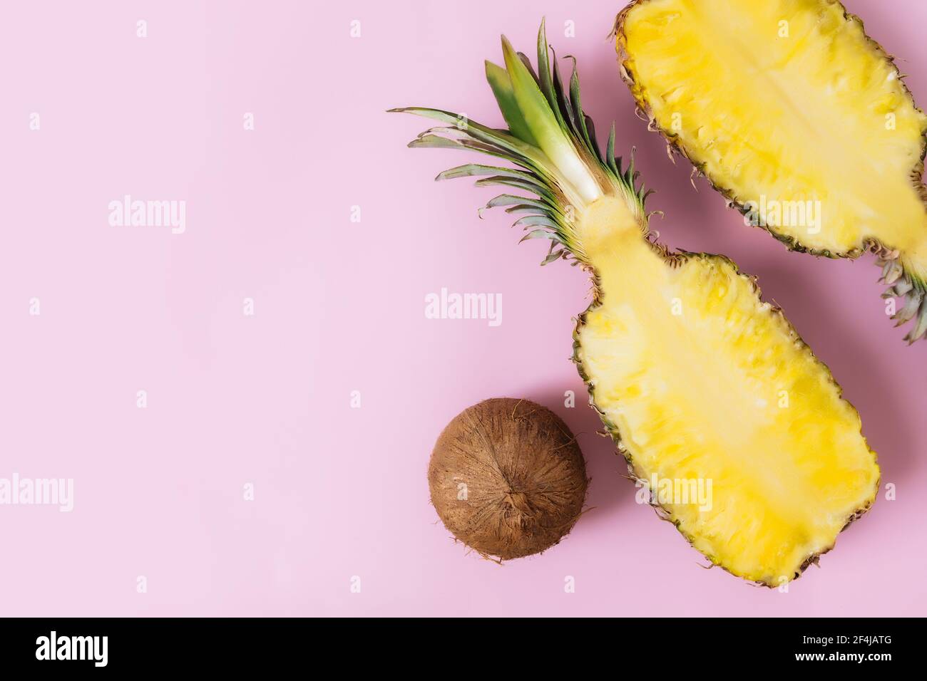Tagliare metà di ananas fresco, cocco su sfondo rosa pastello. Frutta esotica Foto Stock