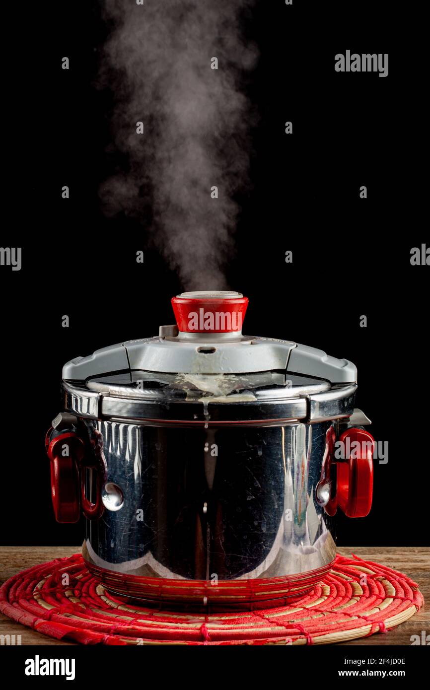 Un fornello a pressione in acciaio si sta raffreddando su un trivet di tessuto su un tavolo di legno. La valvola di pressione viene rilasciata e il vapore fuoriesce quando il sistema si depre Foto Stock
