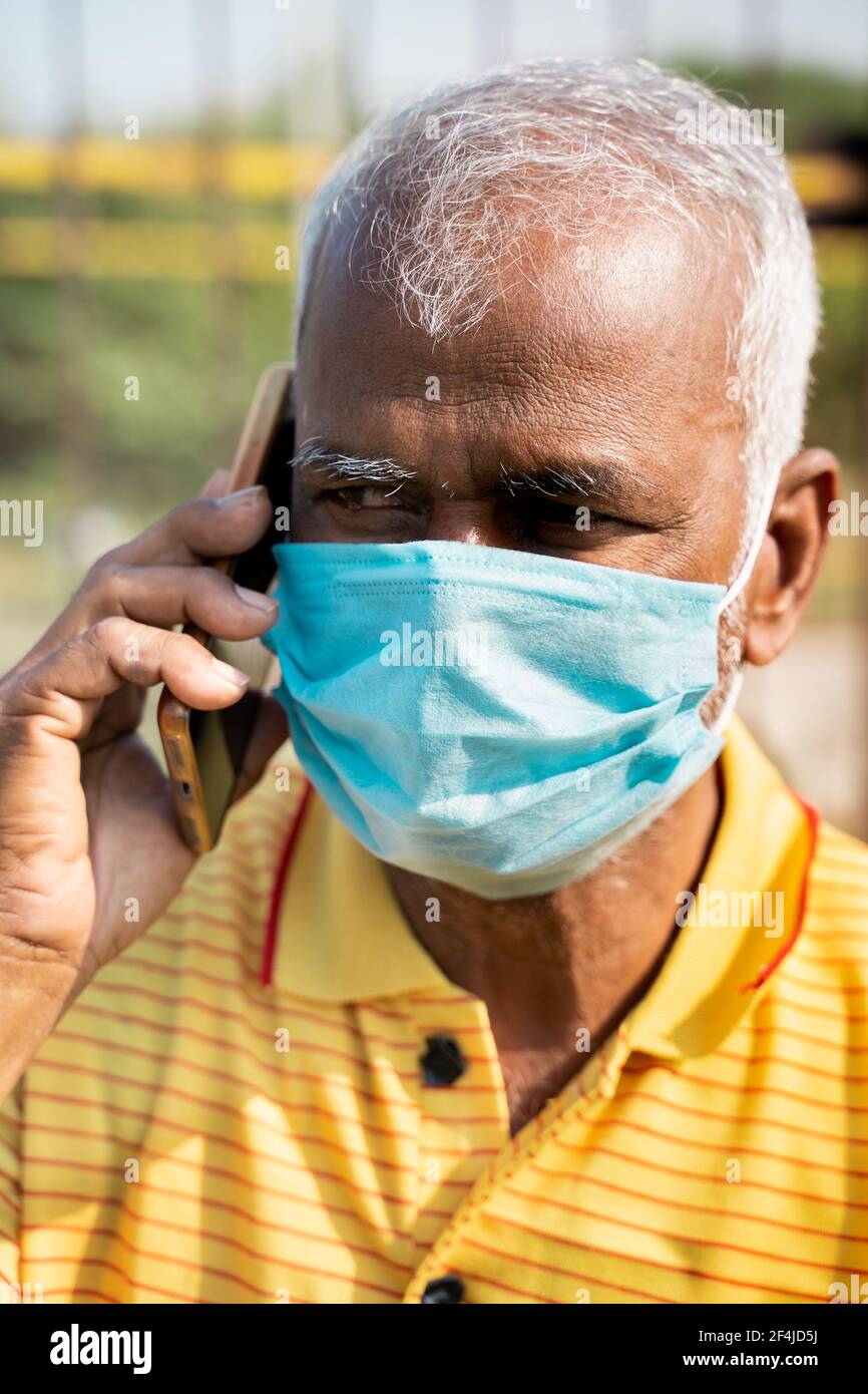 Pan shot di vecchio con maschera medica occupato parlare nel telefono cellulare - concetto di anziani utilizzando la tecnologia, la comunicazione e lo stile di vita. Foto Stock