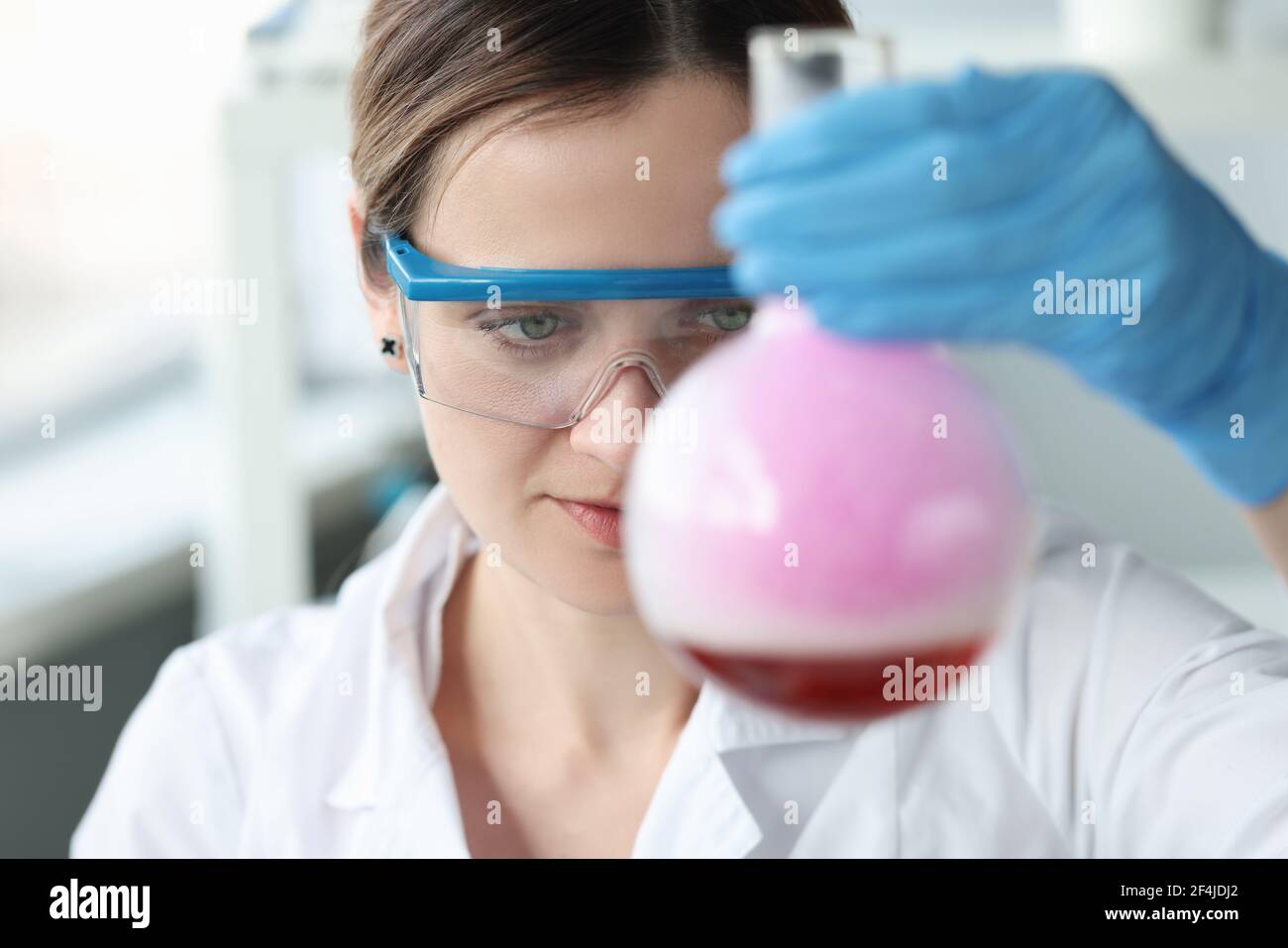 Donna ricercatrice in occhiali sta conducendo esperimenti chimici in fiasca Foto Stock