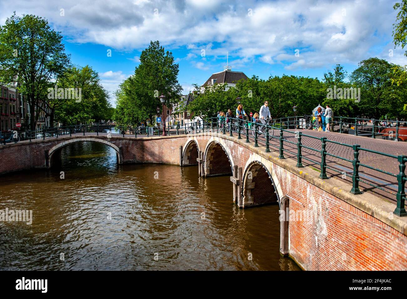 Amsterdam, Paesi Bassi - 7 luglio 2019: Persone che camminano e pedalano su un ponte di mattoni rossi sopra i canali di Amsterdam nei Paesi Bassi Foto Stock