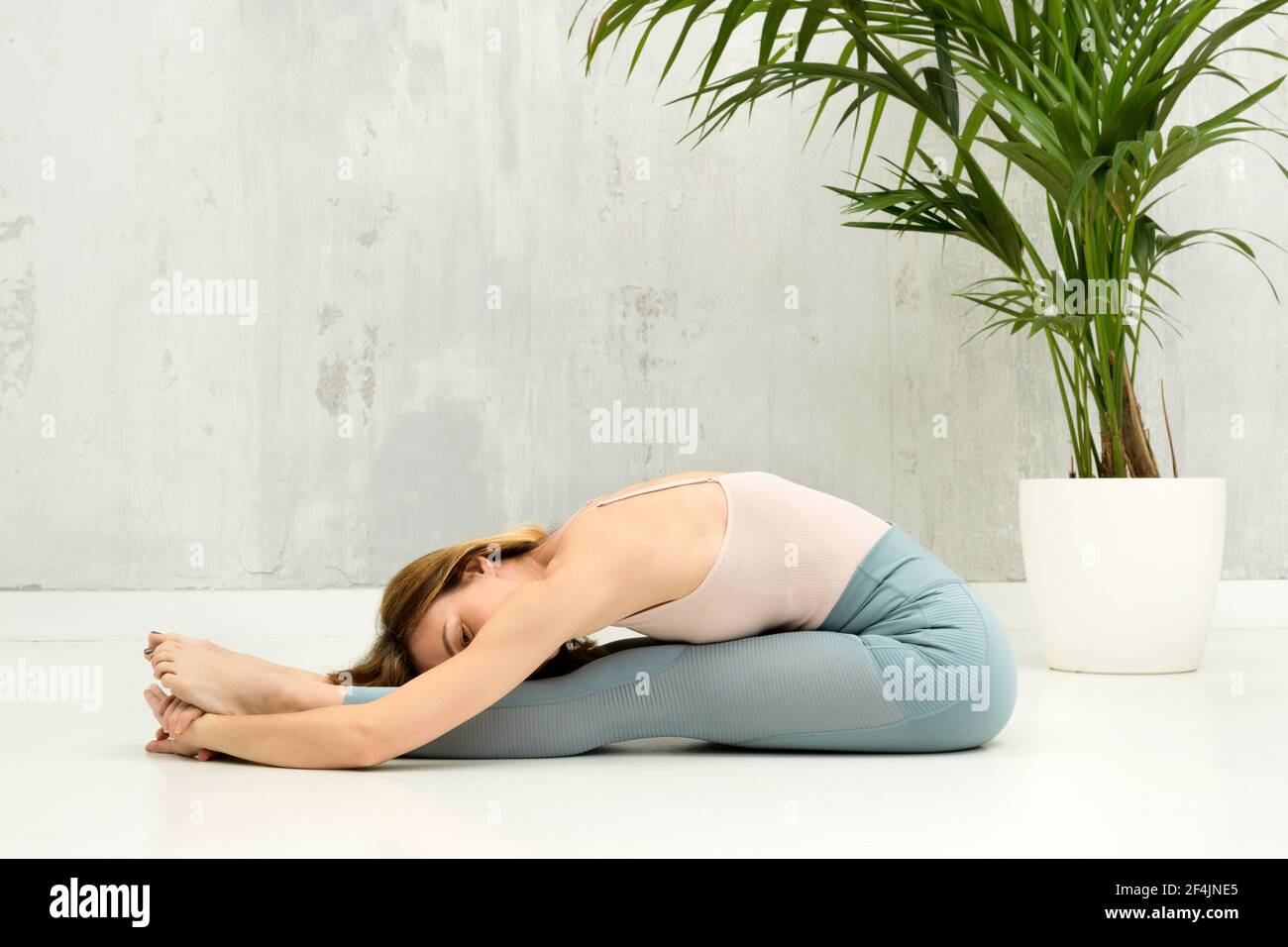 Donna che fa una Pascimottanasana o seduta Forward Bend yoga posa per rilassarsi e allungare le gambe e la colonna vertebrale con copyspace su una parete grigia oltre Foto Stock