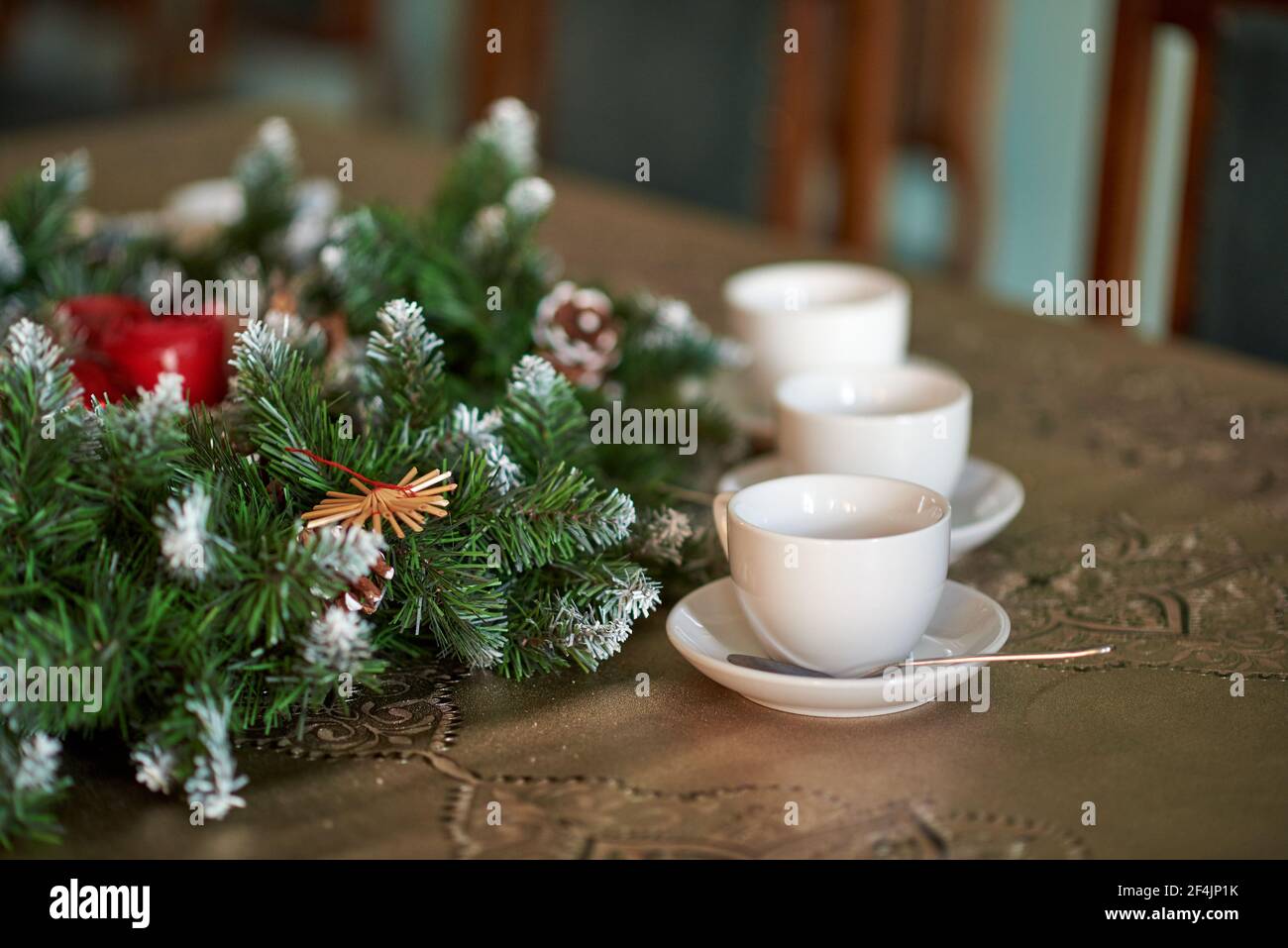 Tre tazze da tè bianche con piattini e cucchiai vicino a coni e rami di abete rosso. Foto Stock