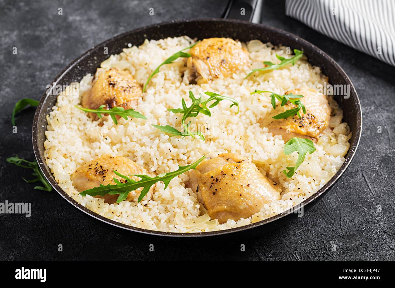 Riso con cosce di pollo, pilaf in padella su fondo scuro. Foto Stock