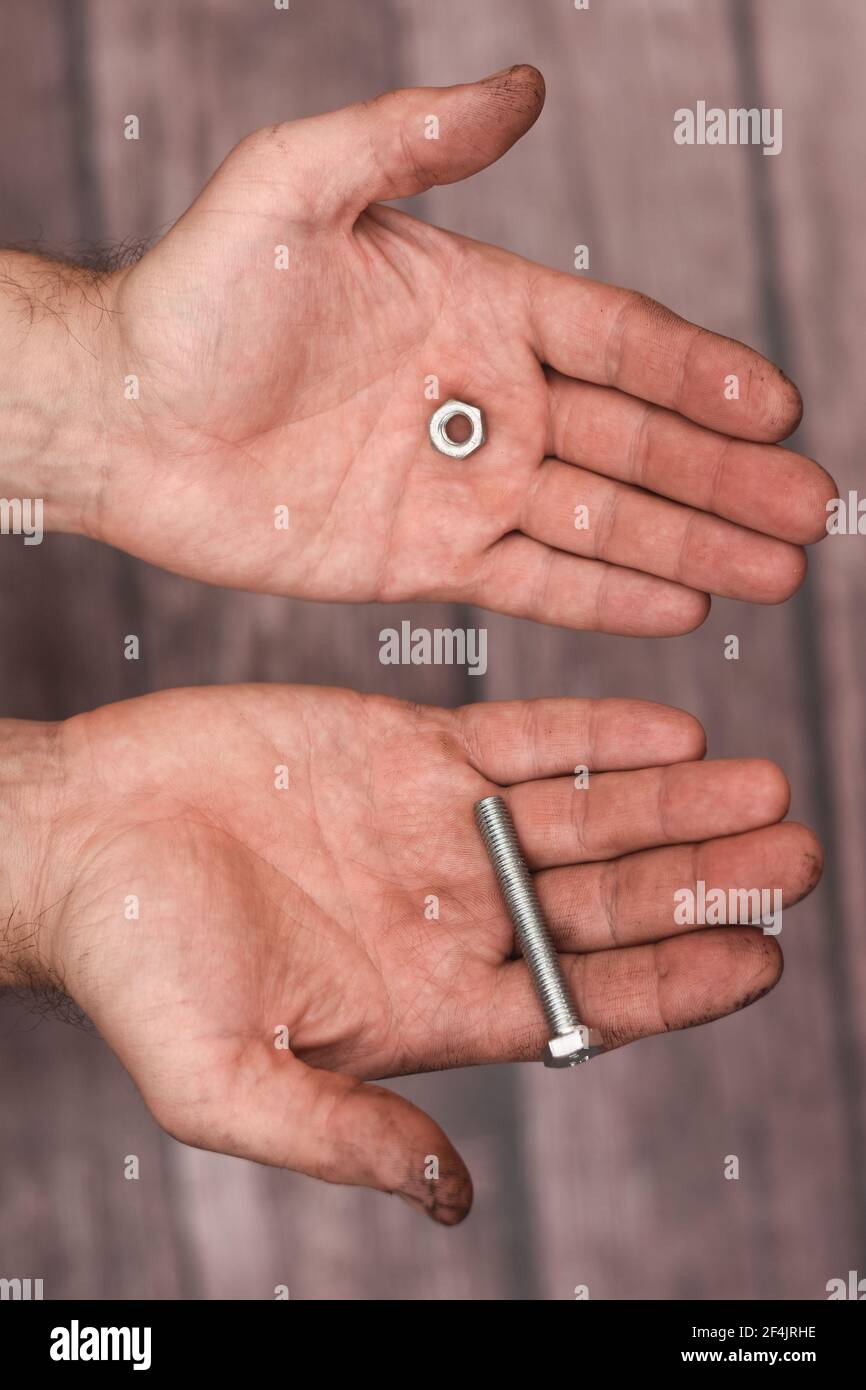 Imbullonare e noci nelle mani degli uomini su uno sfondo di legno. Foto Stock