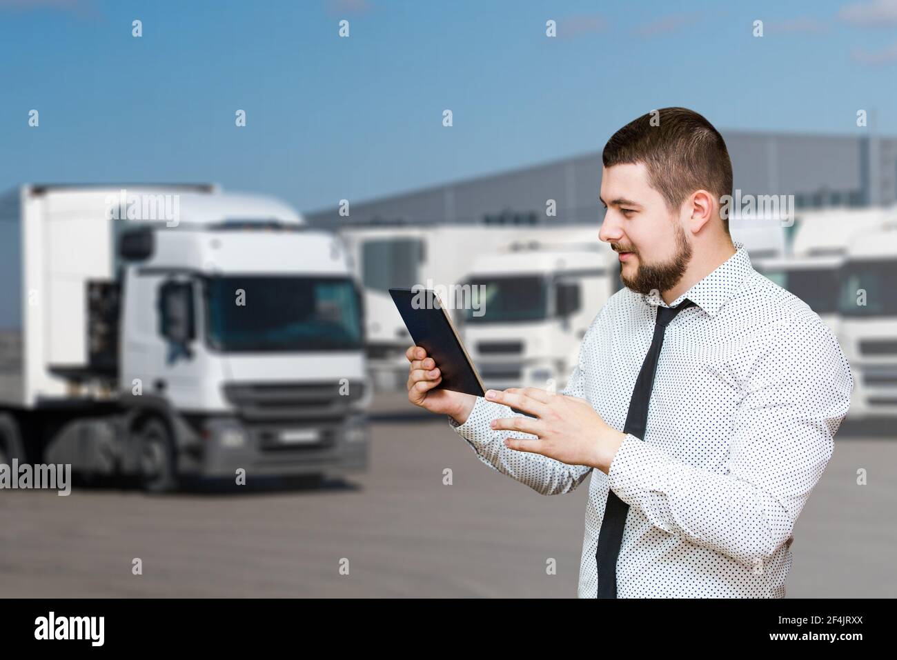 Manager con un tablet digitale sullo sfondo dei veicoli industriali. Gestione della flotta Foto Stock