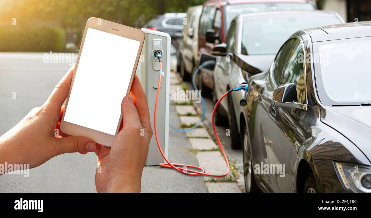 Mani con lo smartphone sullo sfondo di un'auto a noleggio presso la stazione di ricarica per i veicoli elettrici. Condivisione dell'auto. Foto Stock